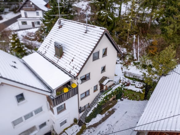 Luftaufnahme eines weißen, dreistöckigen Hauses mit schneebedecktem Dach und Hof in Ravensburg. Ideal für alle, die ein Haus in Ravensburg verkaufen wollen oder sich von einem erfahrenen Immobilienmakler Ravensburg beraten lassen wollen. Umgeben von Bäumen und winterlichem Charme.
