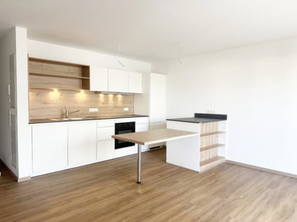 Moderne minimalistische Küche mit weißen Schränken, Holzarbeitsplatten, eingebautem Ofen und offenen Regalen - perfekt für alle, die ein Haus verkaufen Ravensburg. Helles Tageslicht unterstreicht die hölzerne Halbinsel und die hellen Holzböden.