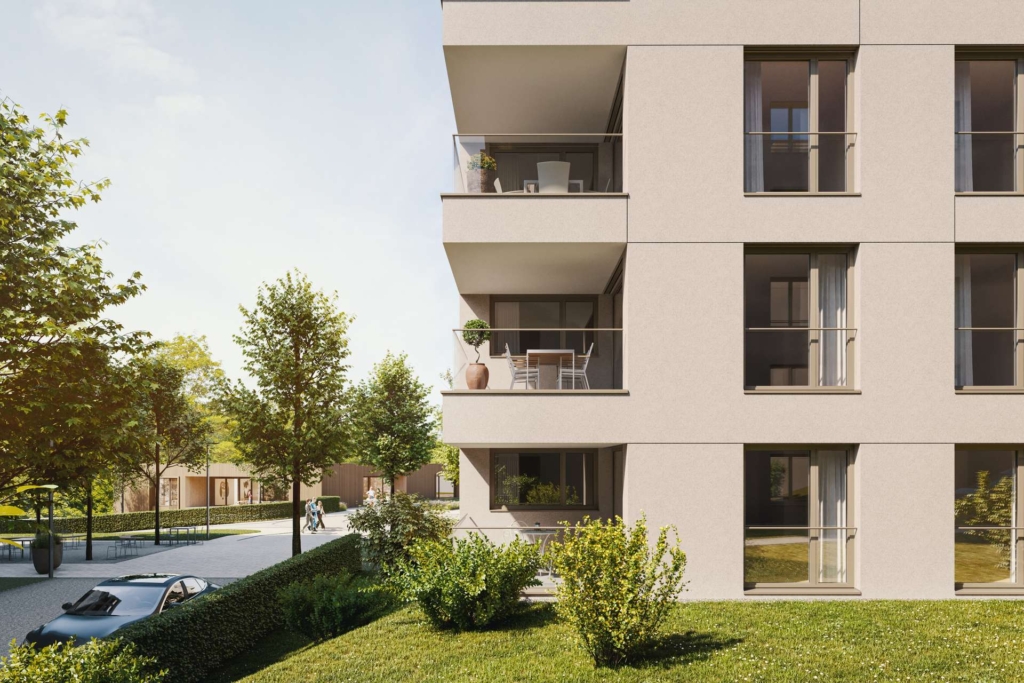 Modernes Wohngebäude mit Balkonen, Terrassenmöbeln und Topfpflanzen. Im Vordergrund befinden sich ein grüner Rasen und Sträucher, links sind Bäume und ein Weg zu sehen, im Hintergrund parkende Autos und weitere Gebäude.