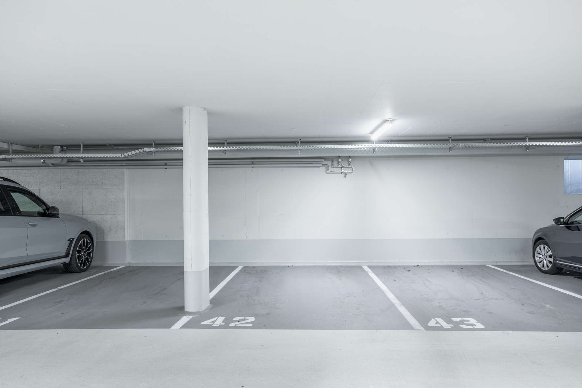 Tiefgarage Die freien Parkplätze Nr. 42 und 43 in einem sauberen Parkhaus, auf deren beiden Seiten jeweils zwei Autos teilweise zu sehen sind.