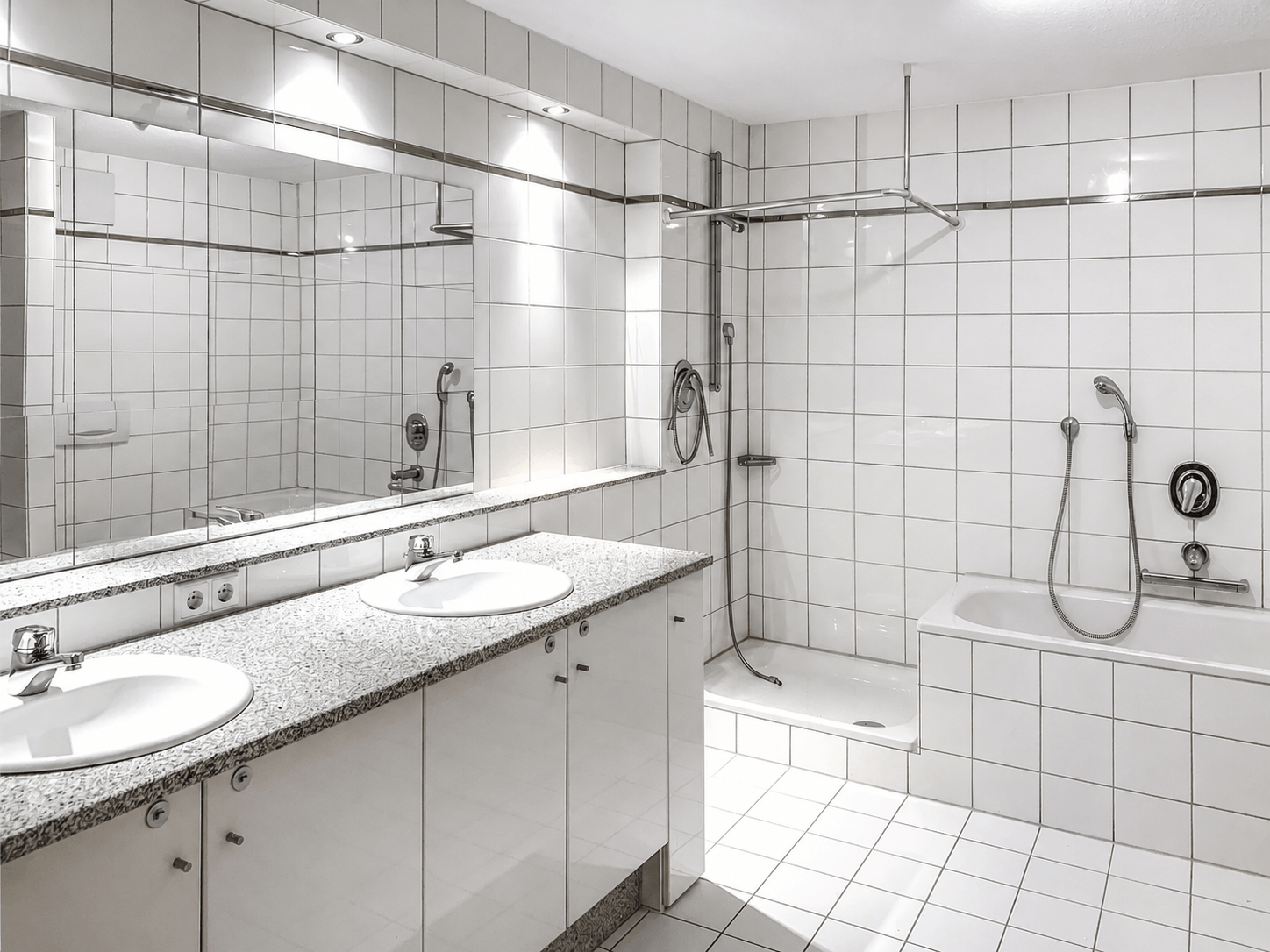Modernes, weißes Badezimmer mit zwei Waschbecken, einem großen Spiegel, einer Badewanne mit Handbrause, einer separaten begehbaren Dusche sowie gefliesten Wänden und Böden.