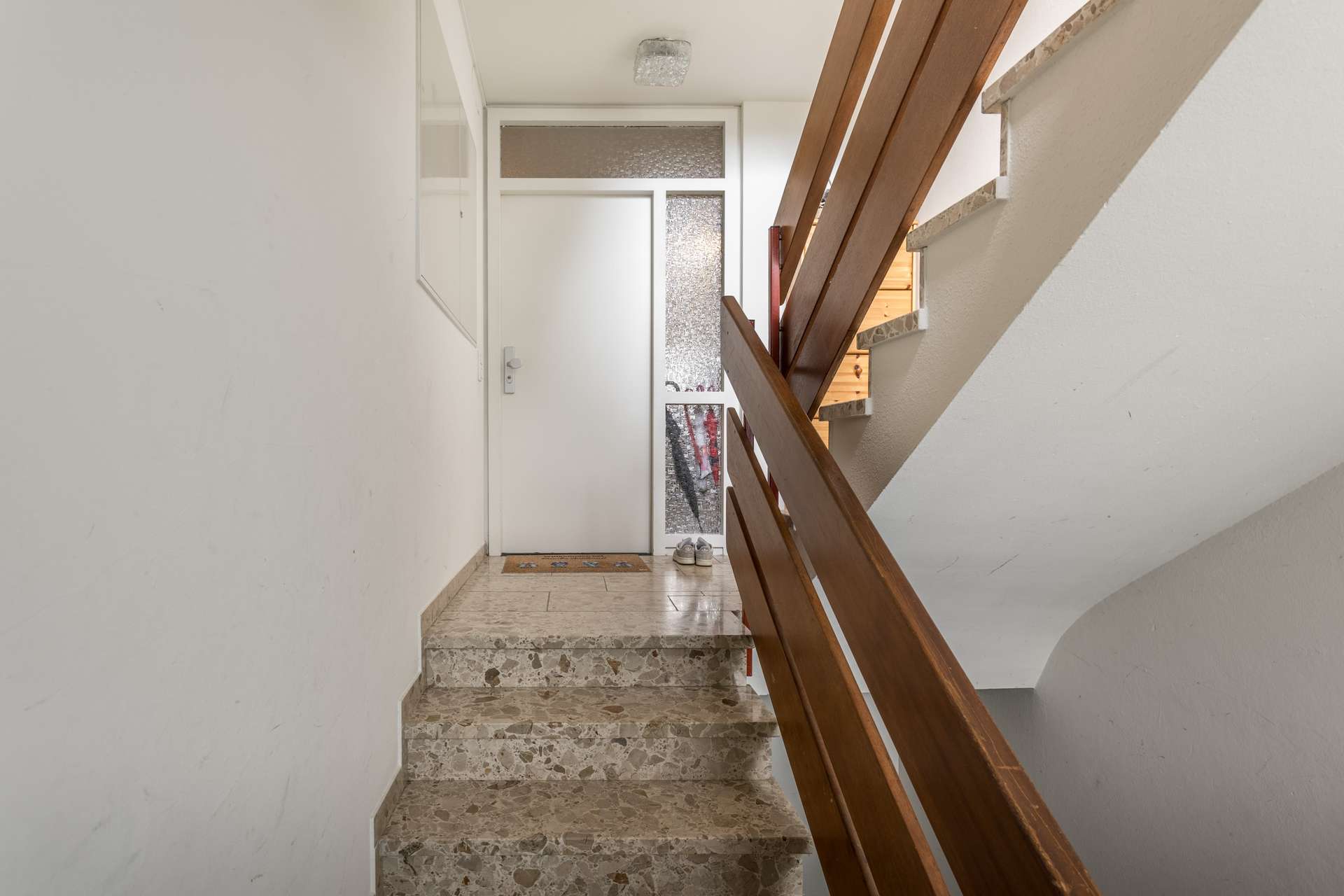 EG Eine kleine Steintreppe, die zu einer weißen Haustür führt, mit einem Holzgeländer auf der rechten Seite.
