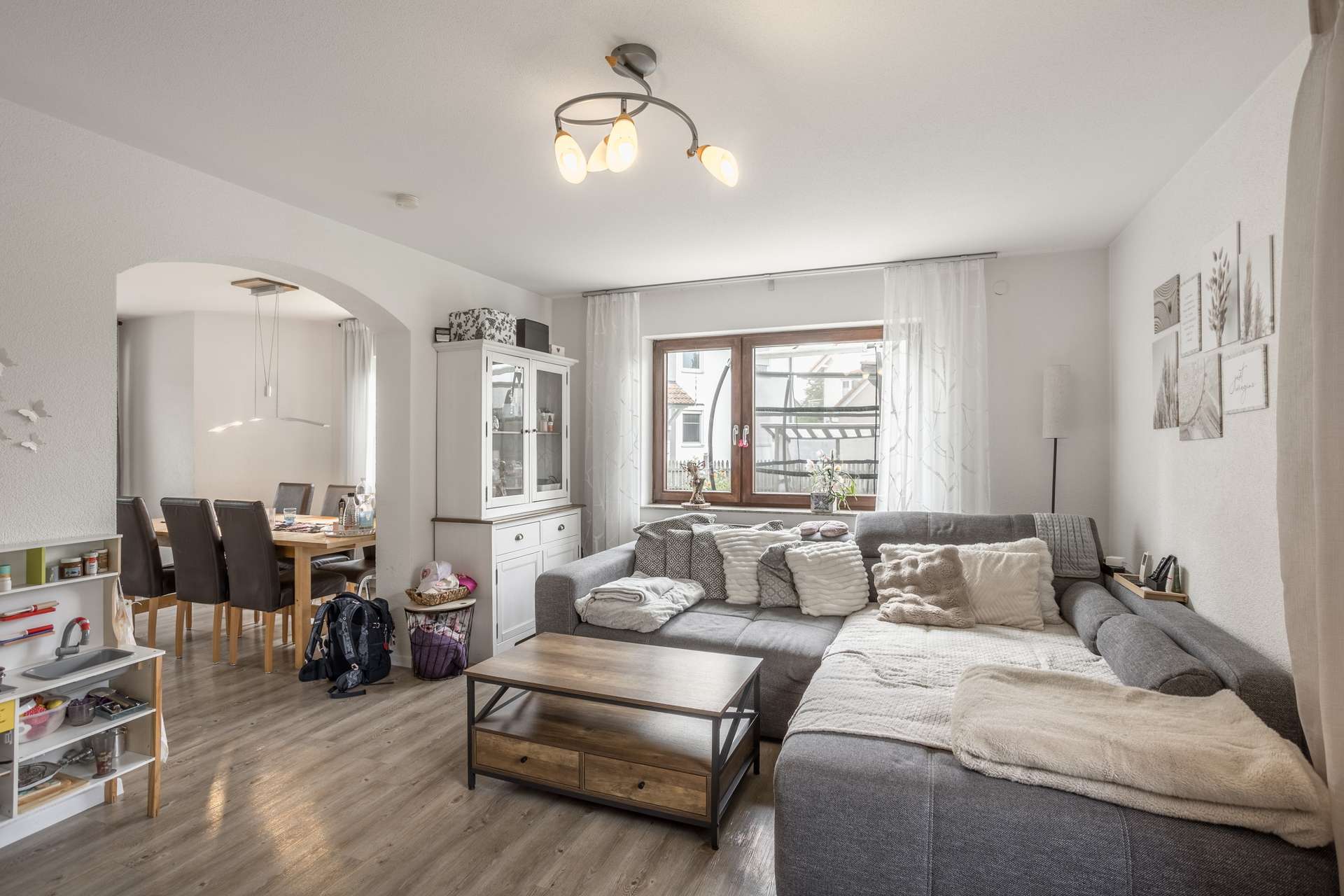 EG Ein Wohnzimmer mit einem großen grauen Ecksofa, einem Couchtisch aus Holz und einem offenen Torbogen, der zum Essbereich führt.