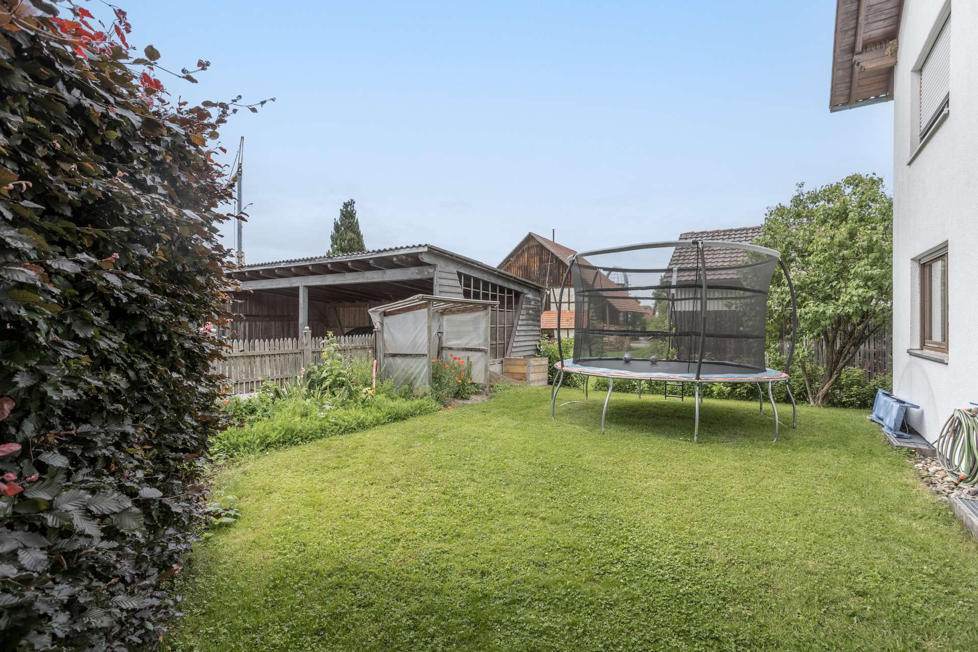 EG Ein Garten mit Rasen, einem Trampolin mit Sicherheitsnetz und einem Holzschuppen.