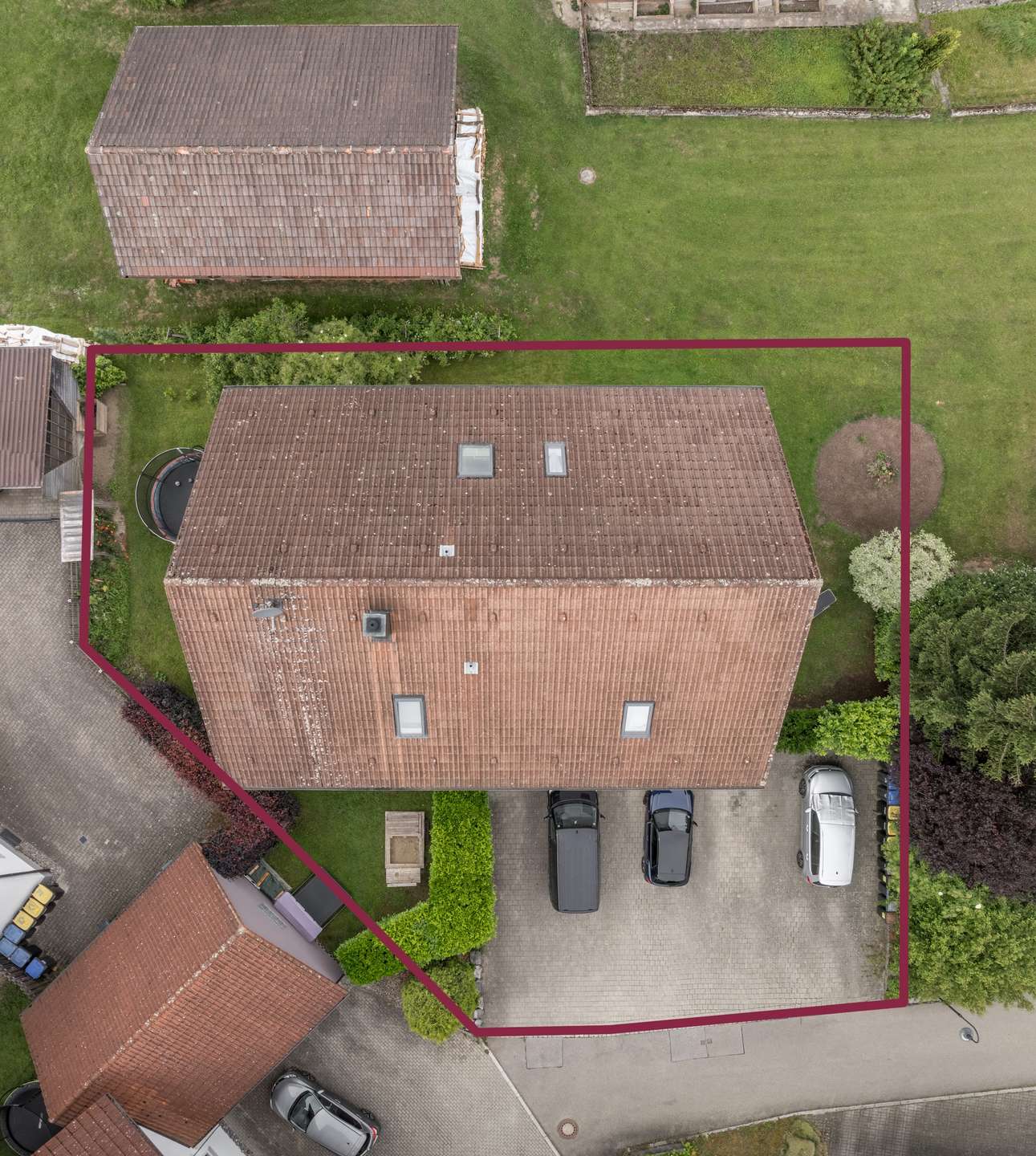 Vogelperspektive Luftaufnahme eines Hauses mit rotem Ziegeldach und einer Einfahrt, auf der drei Autos geparkt sind, umrandet von einem roten Polygon.