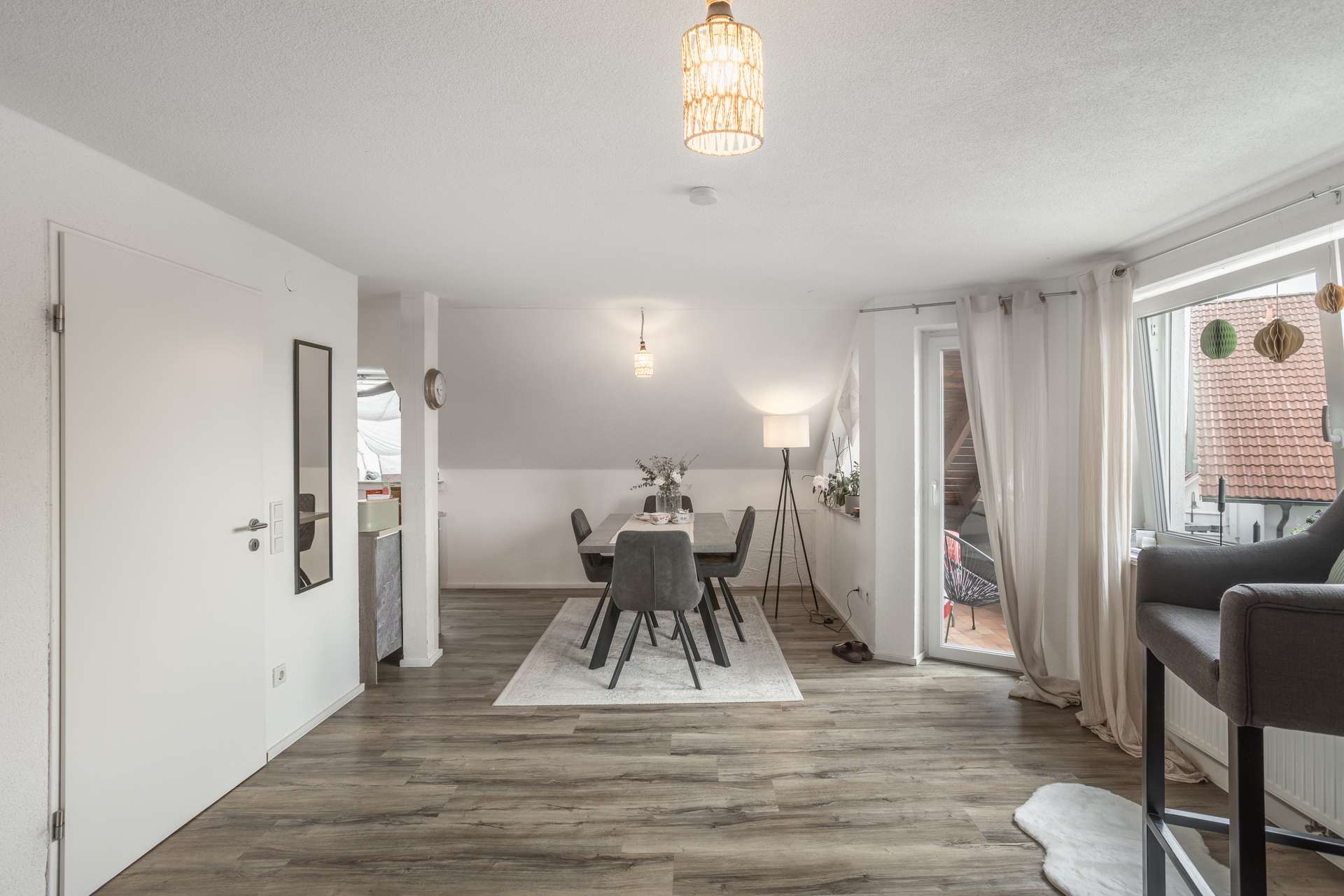 DG Ein Essbereich mit einem Tisch und sechs grauen Stühlen auf einem gemusterten Teppich, der zwischen einer Stehlampe und einer Glastür zum Balkon steht.