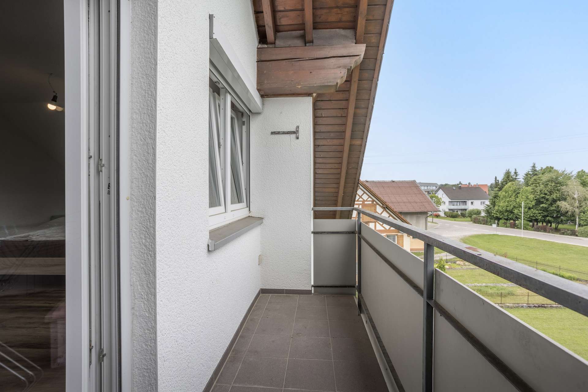 DG Ein schmaler Balkon mit Fliesenboden und einem Metallgeländer, mit Blick auf eine Vorstadtstraße und einen begrünten Garten.