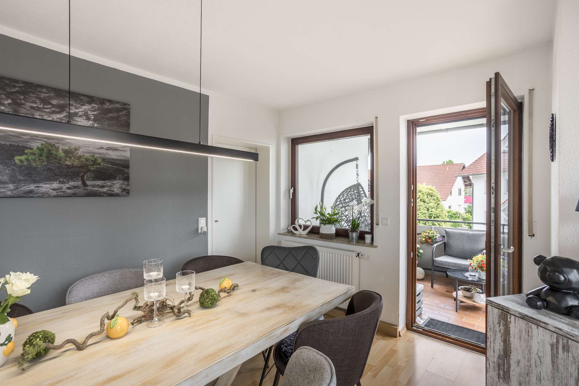 1.OG Ein Esstisch aus hellem Holz mit grauen Stühlen, neben einer offenen Tür, die auf einen Balkon führt.