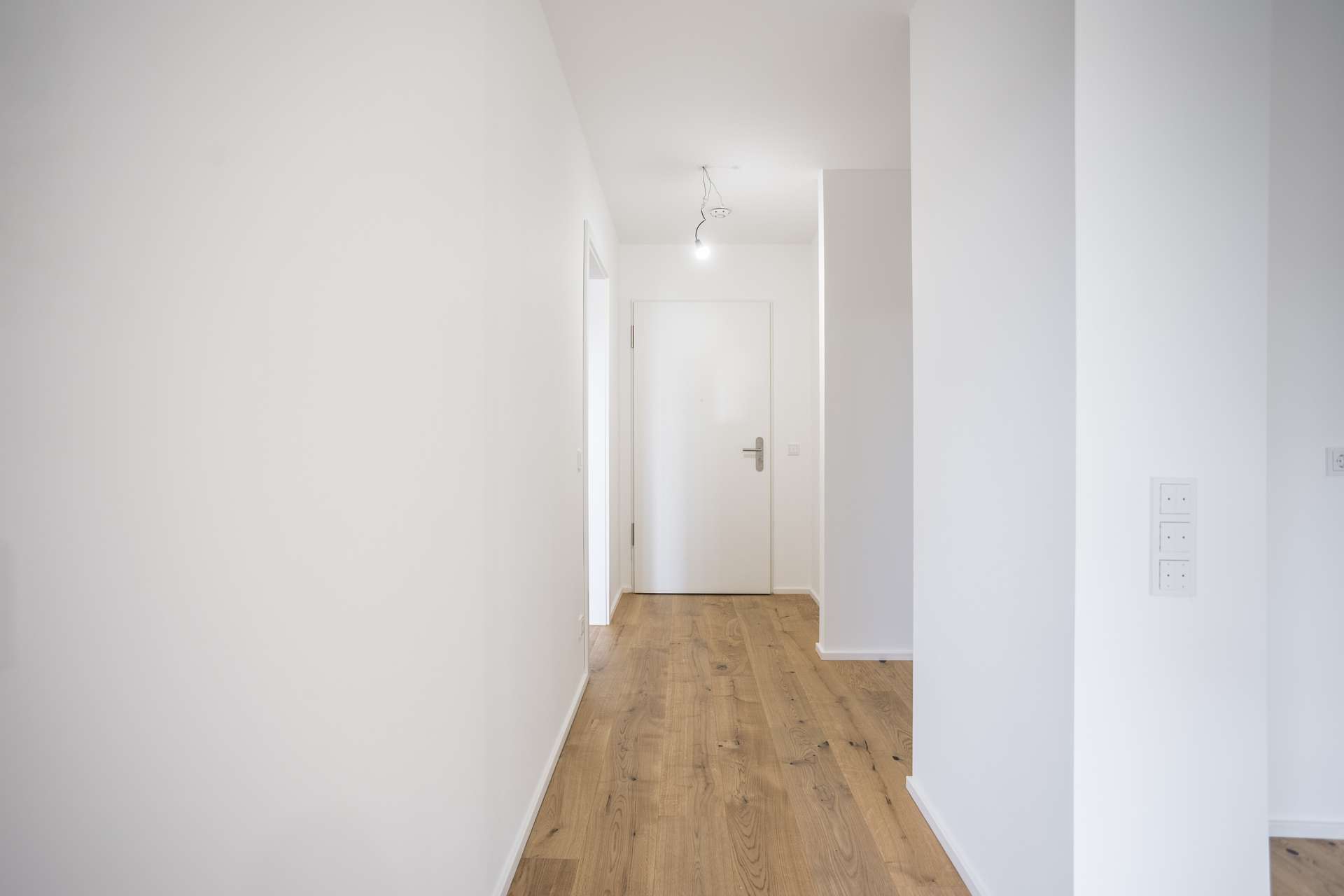 Ein minimalistischer Flur mit weißen Wänden, Holzboden und einer einzigen geschlossenen Tür am Ende. Ein minimalistischer Flur mit weißen Wänden, Holzboden und einer einzigen geschlossenen Tür am Ende.