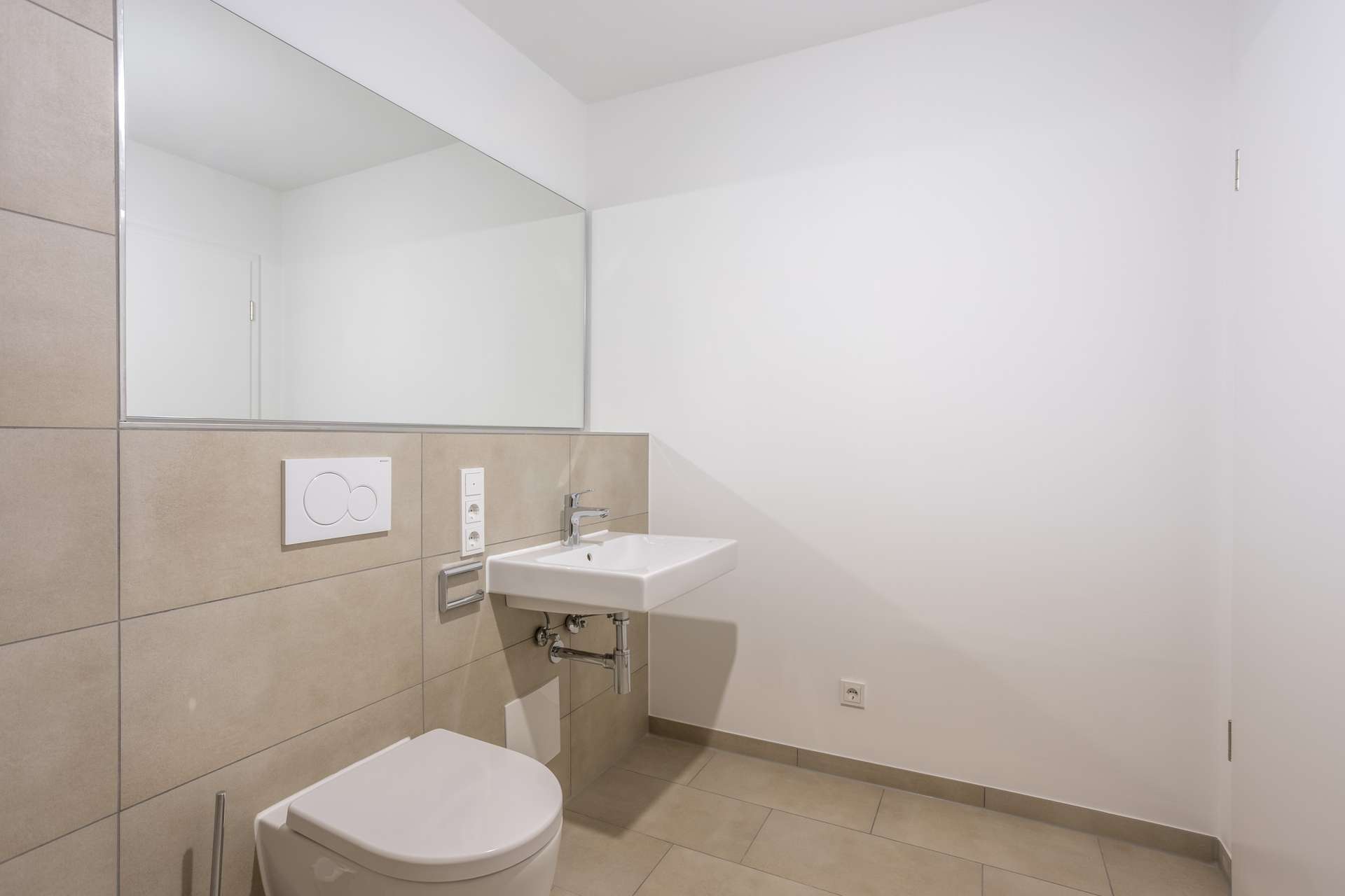 Ein modernes Badezimmer mit einem weißen Wand-WC, einem rechteckigen Waschbecken und einem großen Wandspiegel über den gefliesten Wänden. Ein modernes Badezimmer mit einem weißen Wand-WC, einem rechteckigen Waschbecken und einem großen Wandspiegel über den gefliesten Wänden.