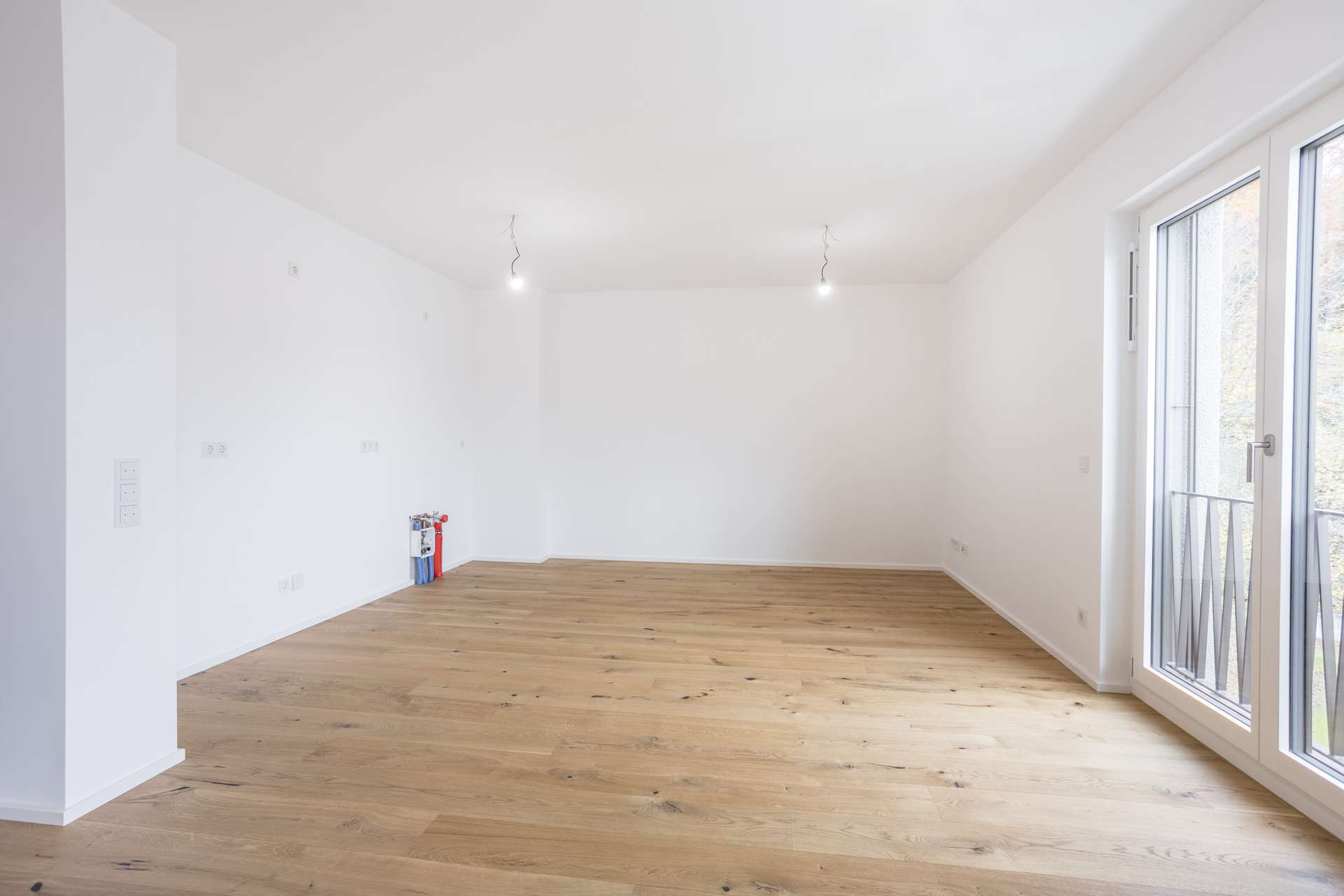 Ein leerer Raum mit weißen Wänden, Holzboden und einer Balkontür. Ein leerer Raum mit weißen Wänden, Holzboden und einer Balkontür.