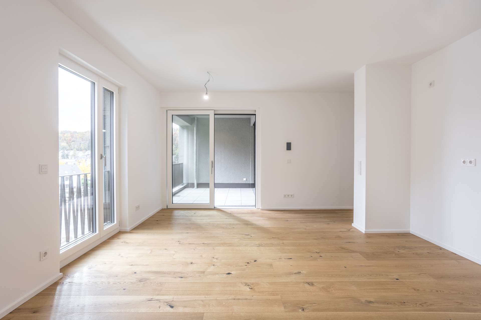 Ein leerer Raum mit weißen Wänden, hellem Holzboden und einer Glasschiebetür, die auf einen Balkon führt. Ein leerer Raum mit weißen Wänden, hellem Holzboden und einer Glasschiebetür, die auf einen Balkon führt.
