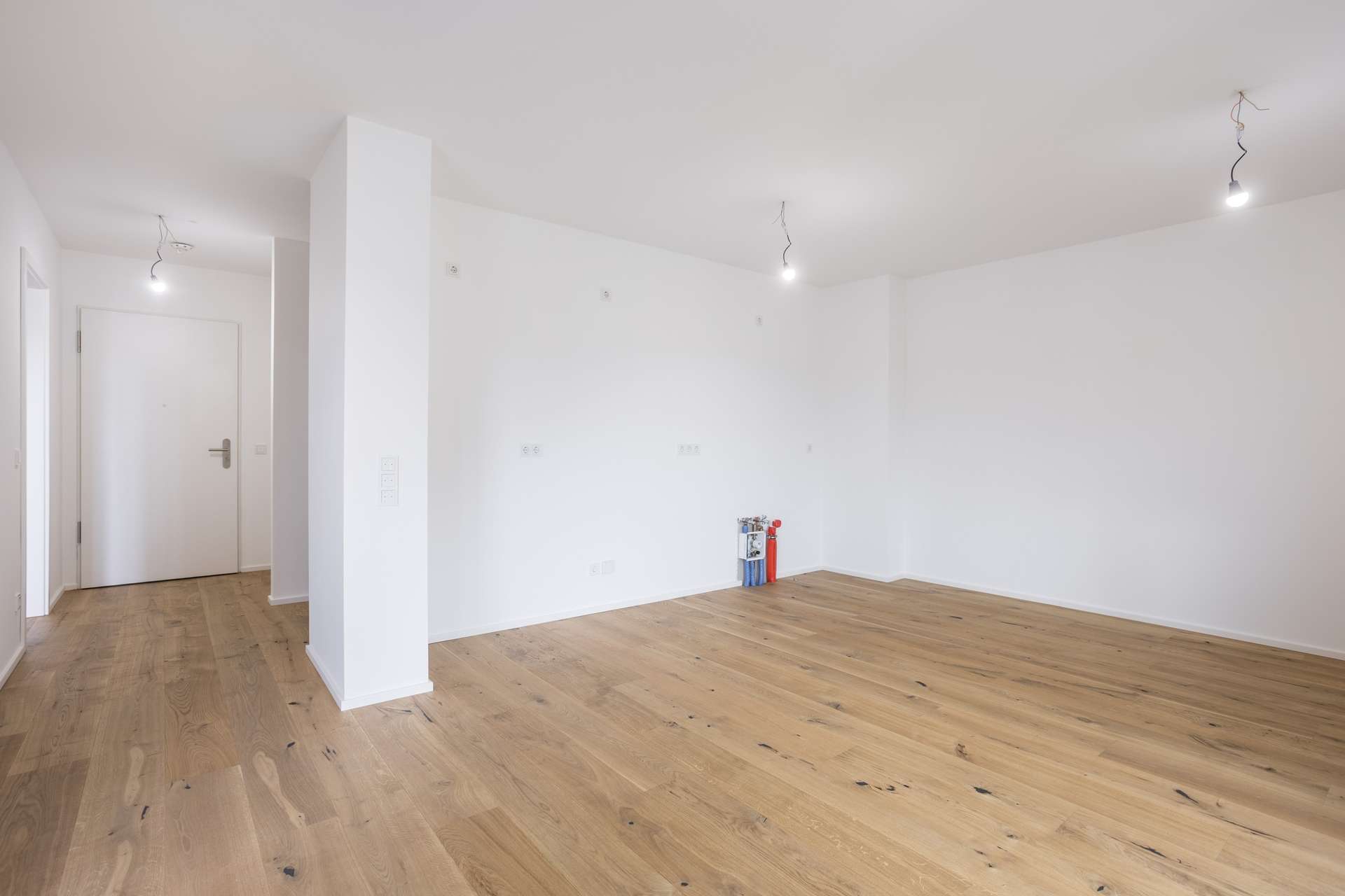 Ein leerer Raum mit weißen Wänden, Holzboden, einer geschlossenen weißen Tür und hängenden Glühbirnen. Ein leerer Raum mit weißen Wänden, Holzboden, einer geschlossenen weißen Tür und hängenden Glühbirnen.