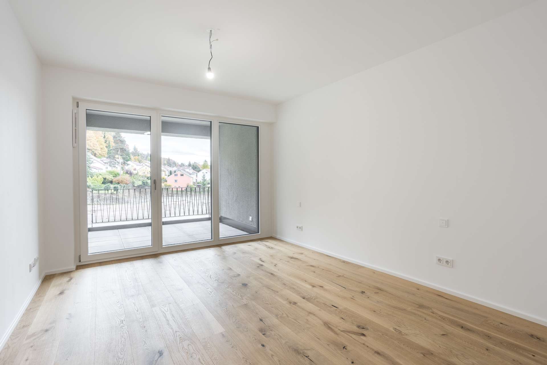 Ein leerer Raum mit weißen Wänden, Holzboden und einer Glasschiebetür, die auf einen Balkon führt. Ein leerer Raum mit weißen Wänden, Holzboden und einer Glasschiebetür, die auf einen Balkon führt.