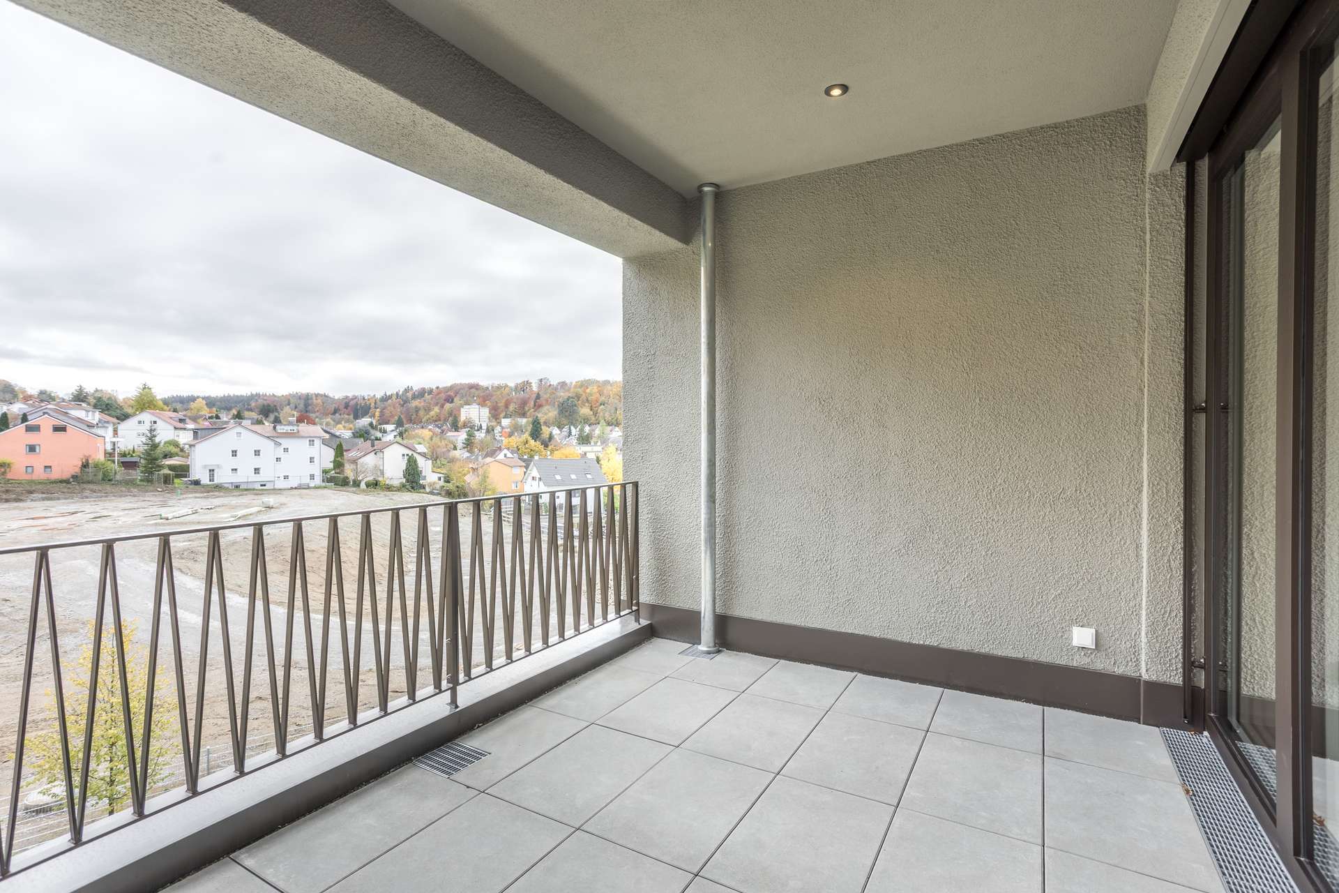 Ein gefliester Balkon mit Metallgeländer, von dem aus man auf ein Vorstadtgebiet und herbstlich gefärbte Bäume blickt. Ein gefliester Balkon mit Metallgeländer, von dem aus man auf ein Vorstadtgebiet und herbstlich gefärbte Bäume blickt.