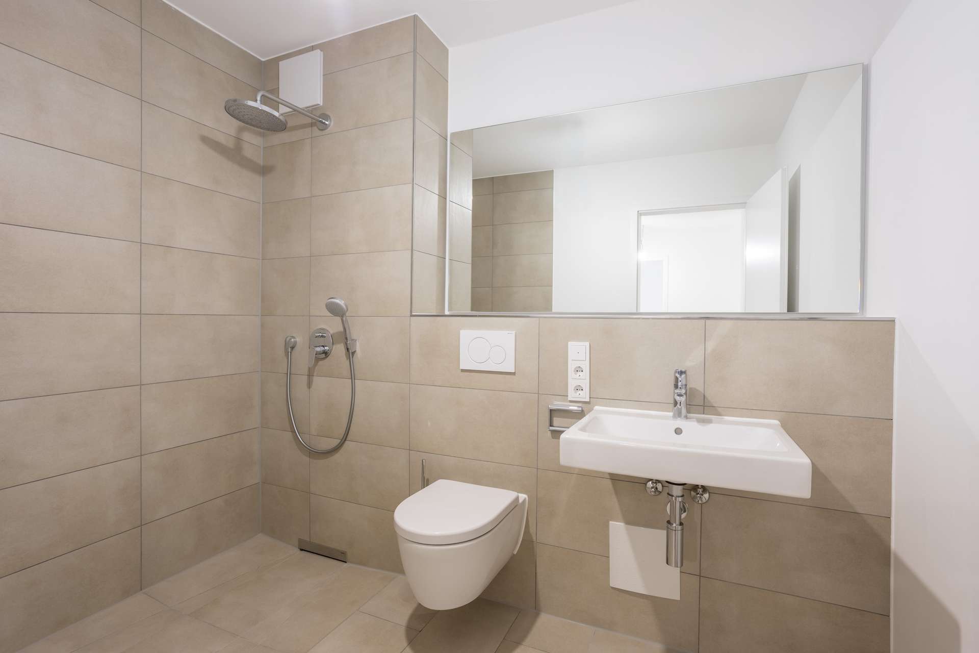 Modernes Badezimmer mit einer gefliesten begehbaren Dusche, einem wandhängenden WC und einem weißen Waschbecken, über dem ein großer Spiegel hängt. Modernes Badezimmer mit einer gefliesten begehbaren Dusche, einem wandhängenden WC und einem weißen Waschbecken, über dem ein großer Spiegel hängt.